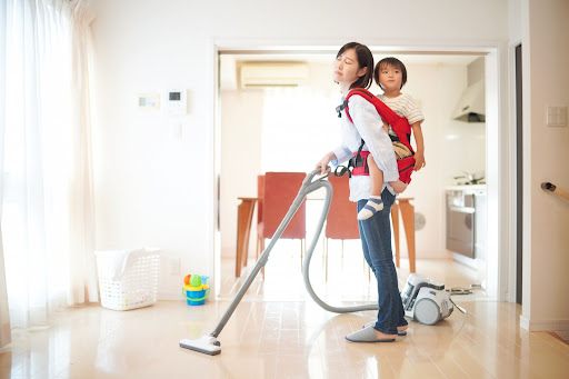 子どもをおんぶしながら掃除機をかけるママ