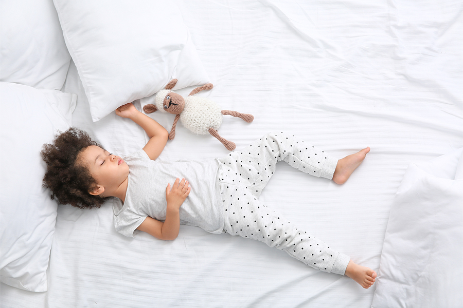 ベッドの上でぬいぐるみと寝る子どもの写真