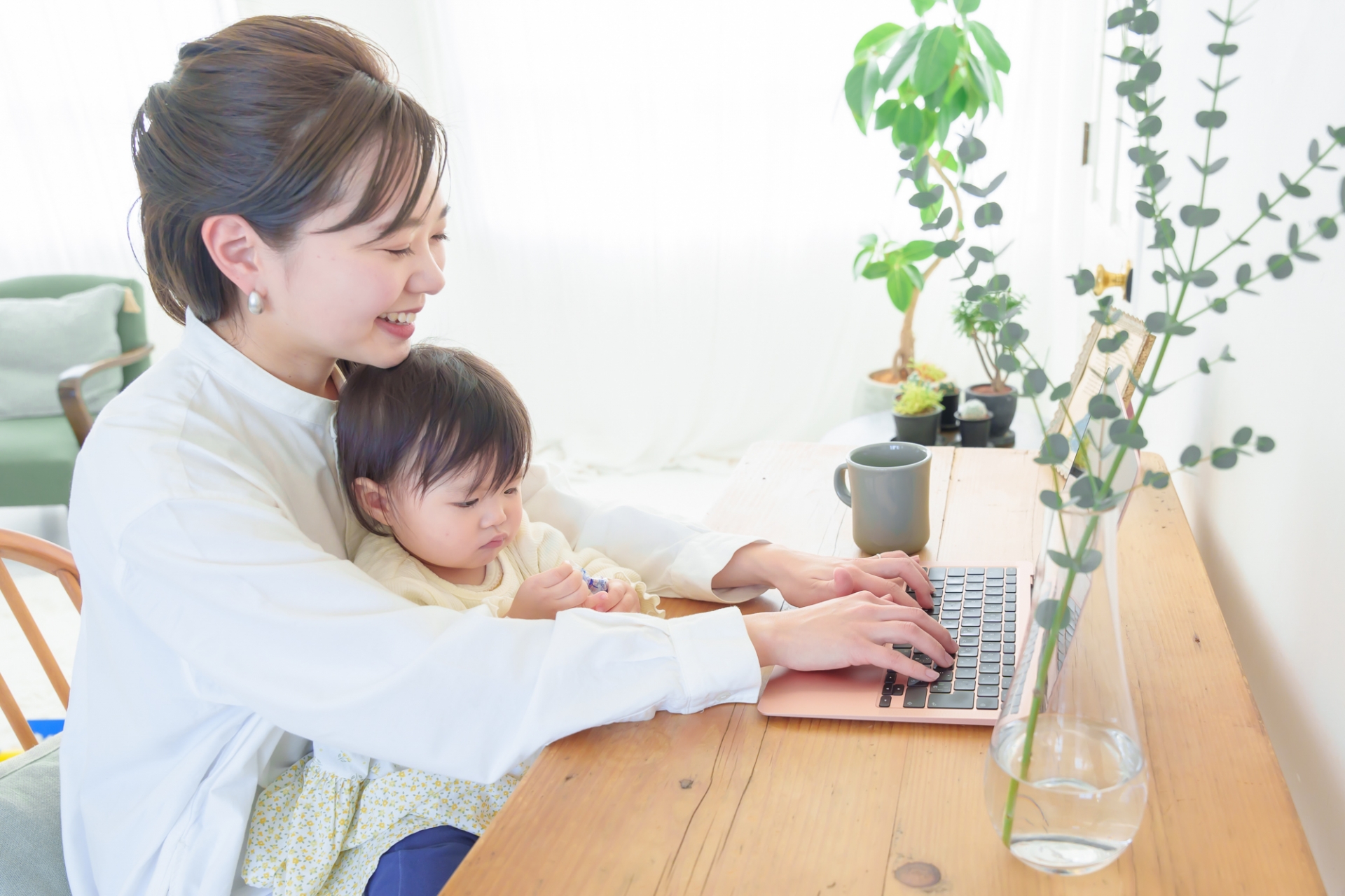 子どもを抱っこしパソコン作業をするママ