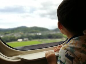 新幹線の窓から外を眺める男の子